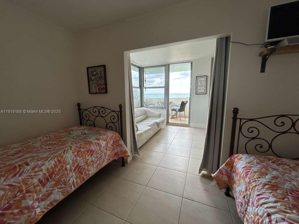 A bedroom with two twin beds and a tiled floor opens onto a balcony overlooking water — 2899 Collins Ave # 625, Miami Beach FL 33140, MIAMI BEACH, FL