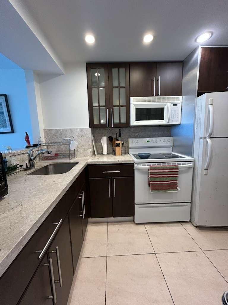 A kitchen features dark wood cabinets, white appliances, and light-colored countertops with a tile floor — 2899 Collins Ave # 625, Miami Beach FL 33140, MIAMI BEACH, FL