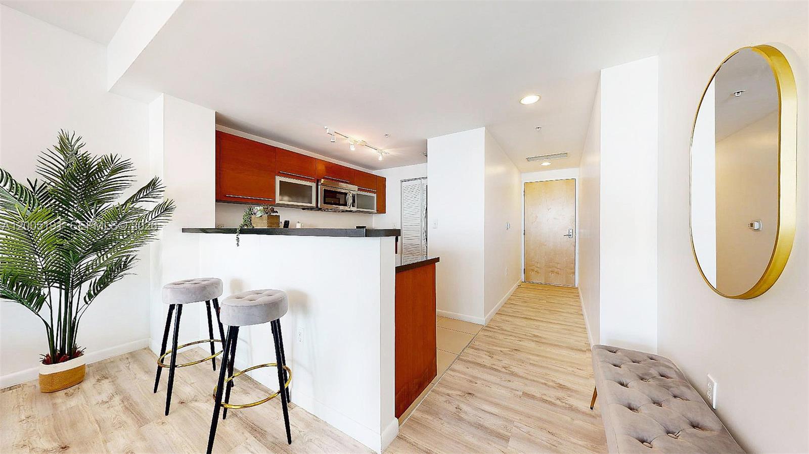 A kitchen with wood cabinets and a breakfast bar overlooks a hallway with a mirror — 244 Biscayne Blvd # 704, Miami FL 33132, MIAMI, FL