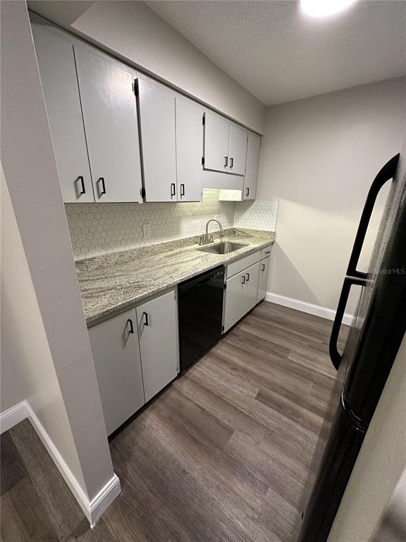 A galley kitchen features gray cabinets, granite countertops, a black dishwasher, and wood-look flooring — 165 PICARDY VILLA CIRCLE UNIT 202, BRANDON, FL
