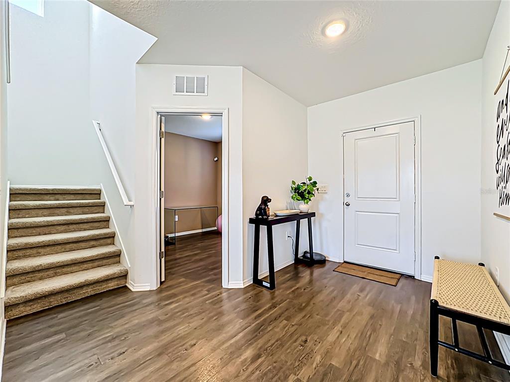 An entryway features wood-look flooring, a carpeted staircase, a white front door, and a console table — 13019 BLUFF OAK WAY, PARRISH, FL