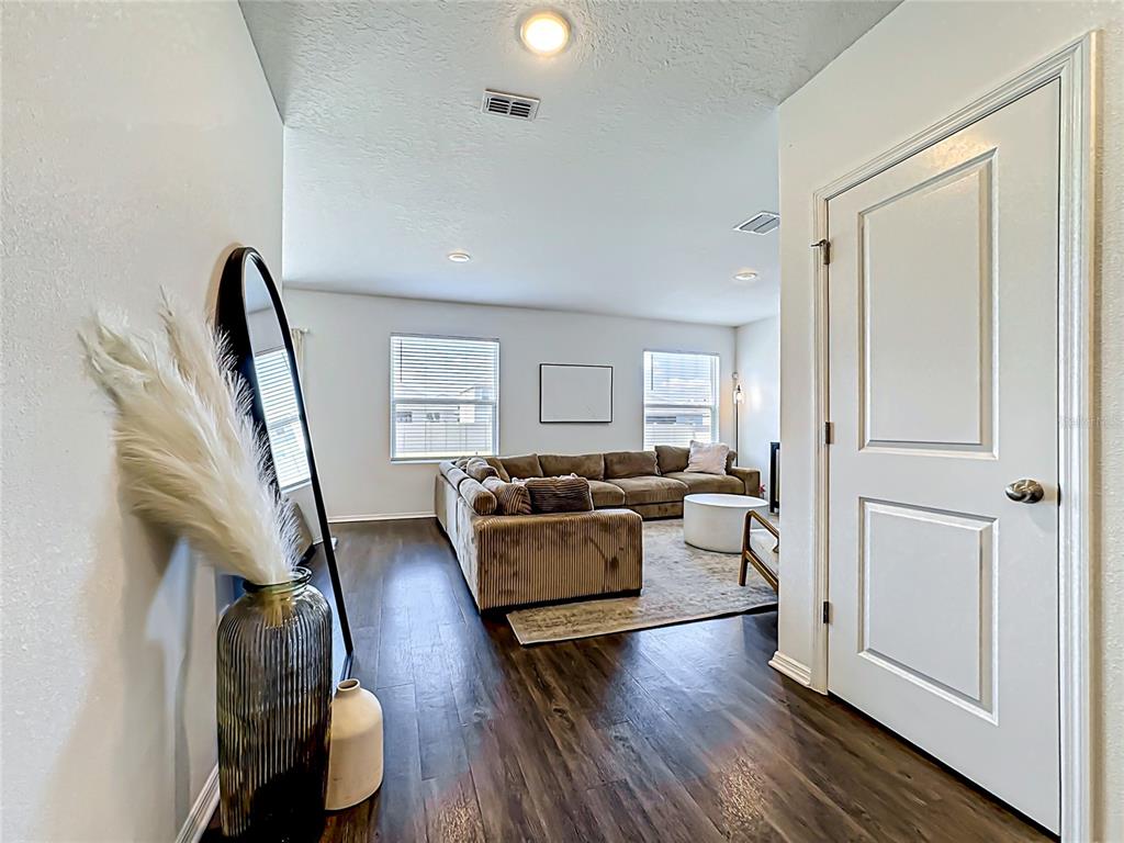 A view from a hallway into a living room with dark wood floors and a sectional — 13019 BLUFF OAK WAY, PARRISH, FL