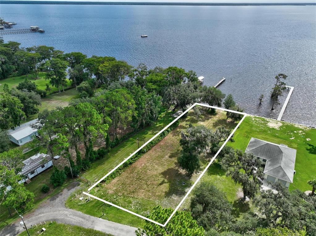 An aerial view shows a rectangular vacant lot situated along a lakefront with trees — 100 SANDRA LANE, CRESCENT CITY, FL