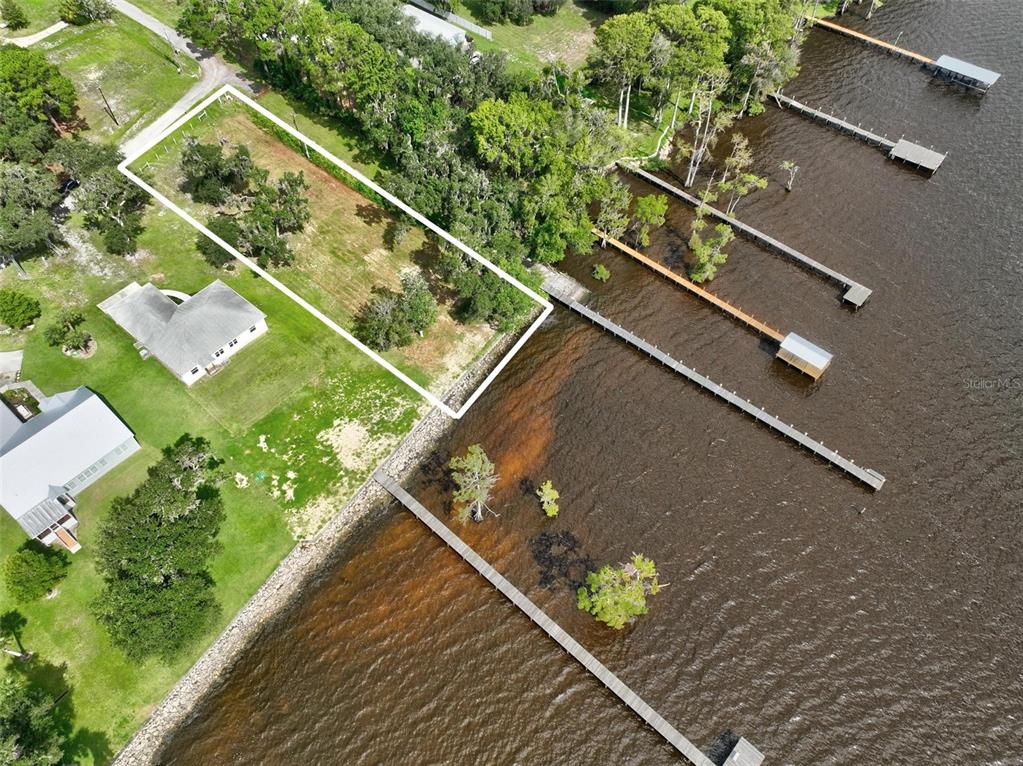 An aerial view shows a vacant waterfront lot outlined in white next to existing homes — 100 SANDRA LANE, CRESCENT CITY, FL