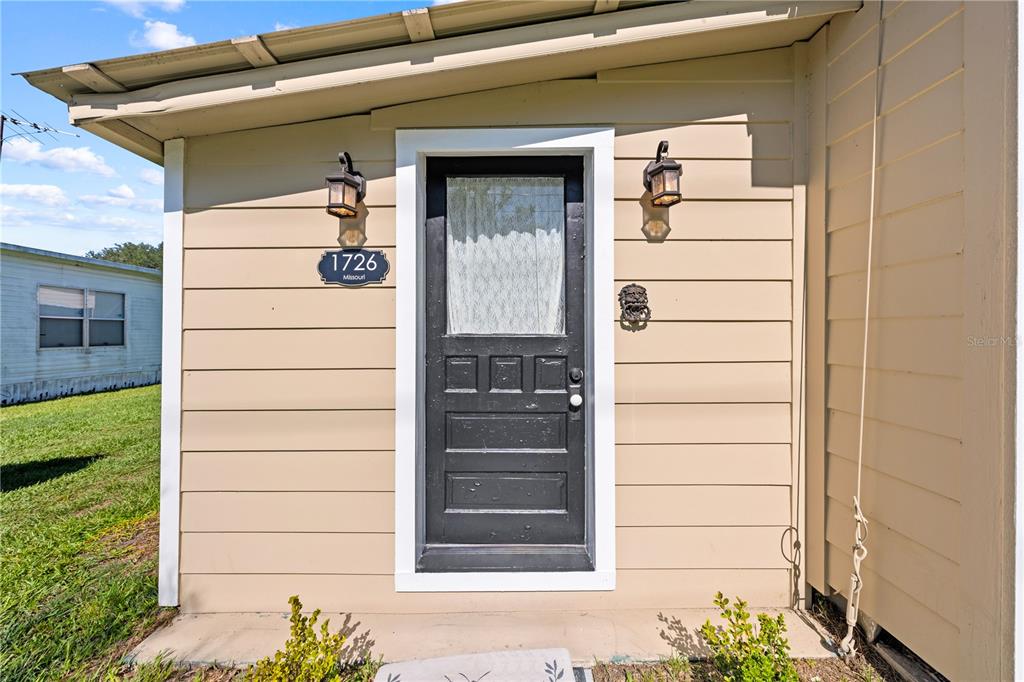 The exterior of a house features beige horizontal siding, a black door, and two wall-mounted lanterns — 1726 MISSOURI AVENUE, ST CLOUD, FL