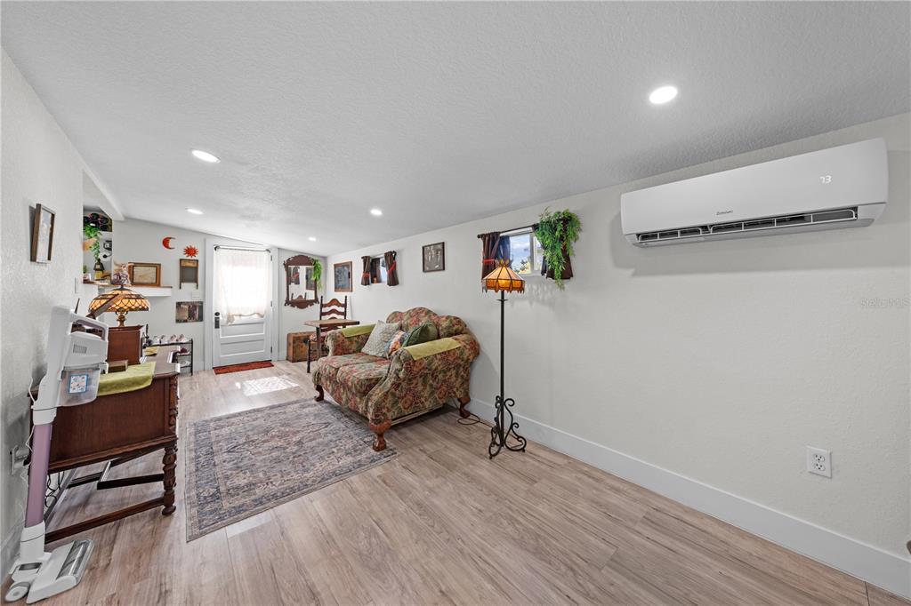 A living room features wood-look flooring, a floral sofa, and a wall-mounted air conditioning unit — 1726 MISSOURI AVENUE, ST CLOUD, FL