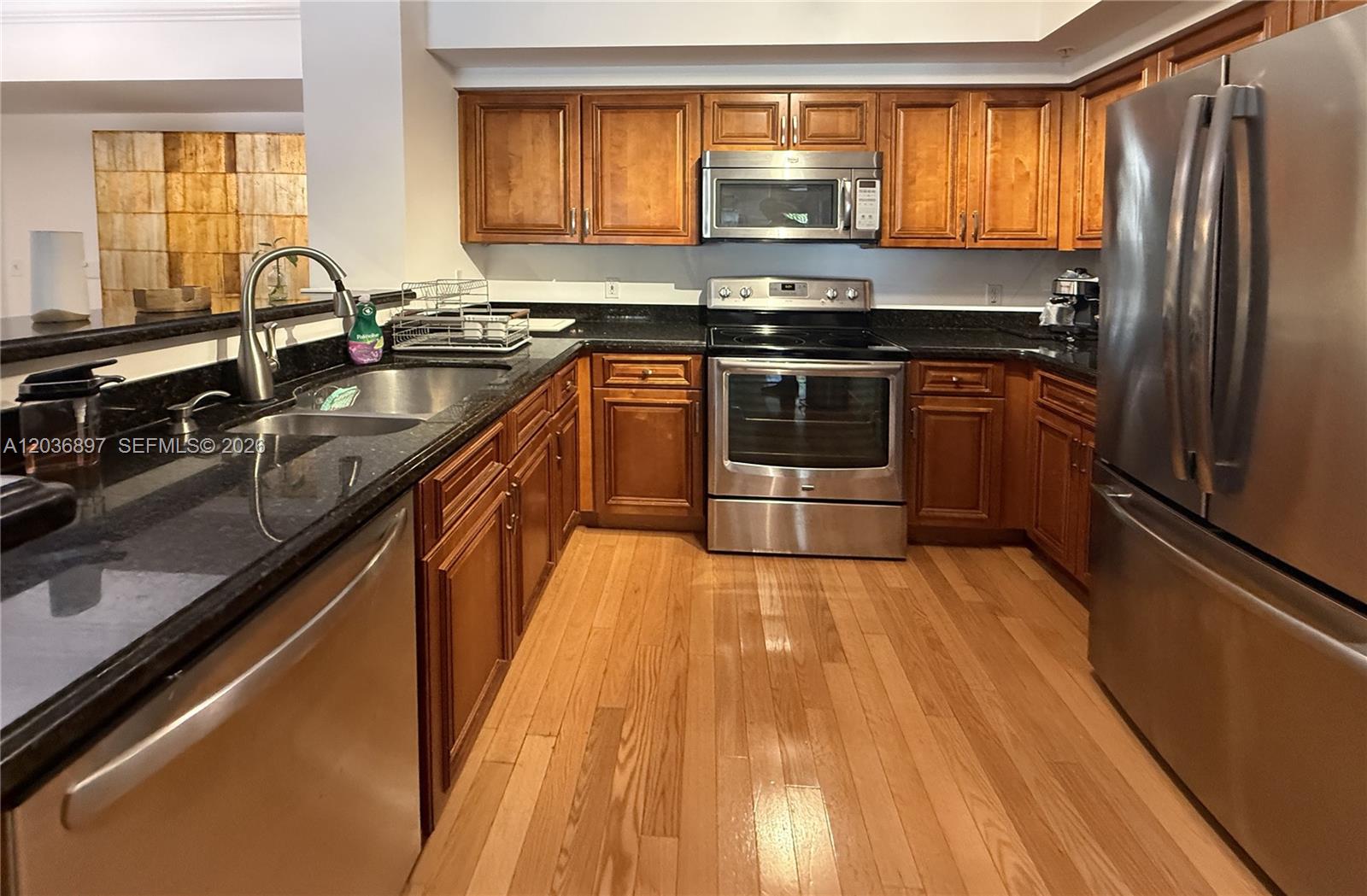 A kitchen features wood cabinets, stainless steel appliances, and black countertops over hardwood floors — 1900 Van Buren St # 317B, Hollywood FL 33020, HOLLYWOOD, FL