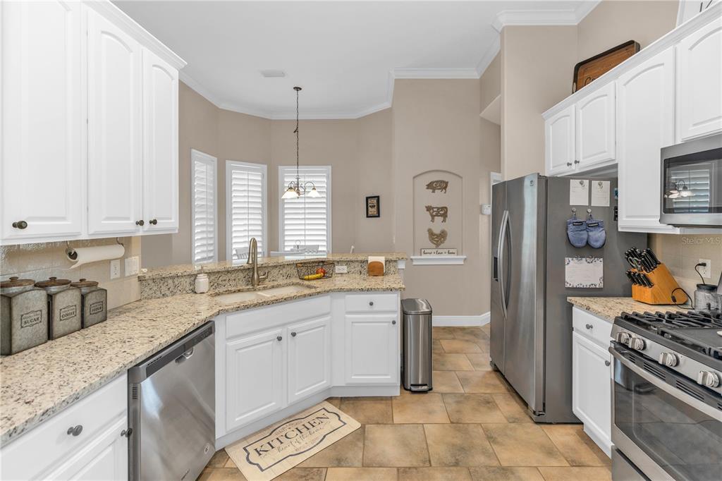 A kitchen features white cabinets, granite countertops, stainless steel appliances, and tile flooring — 325 HAZELTINE DRIVE, DEBARY, FL