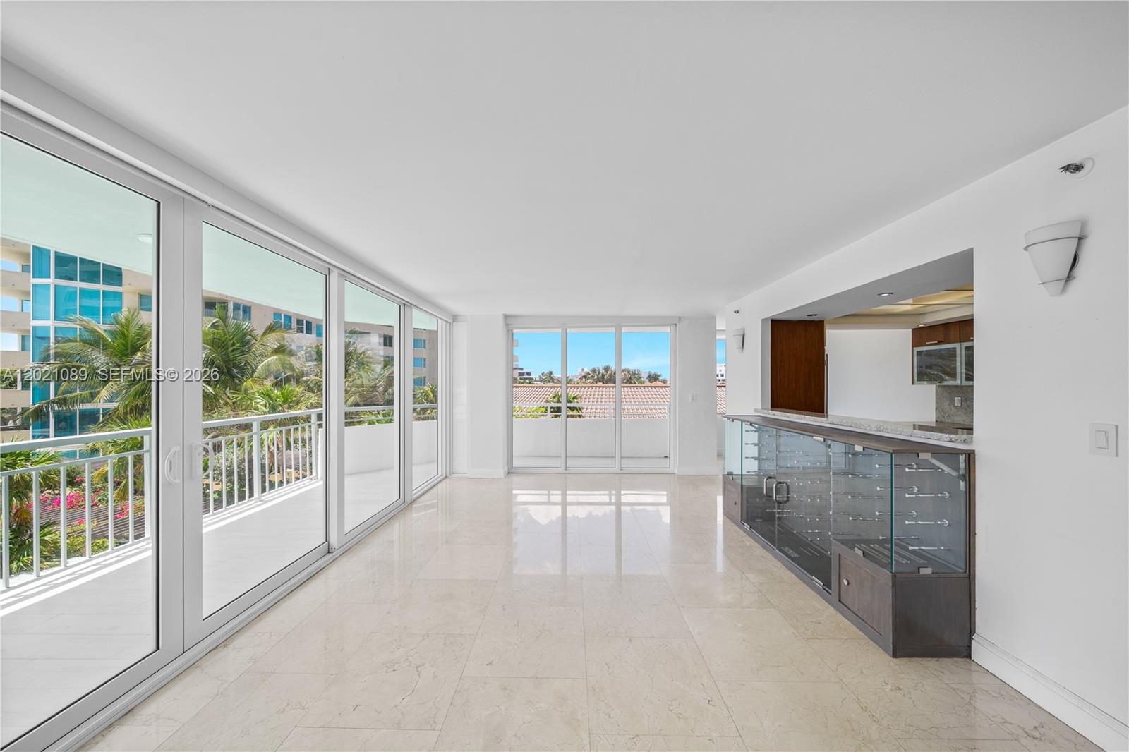 A bright, empty living area features marble floors, floor-to-ceiling glass doors, and a glass-enclosed bar — 400 S Pointe Dr # 409, Miami Beach FL 33139, MIAMI BEACH, FL