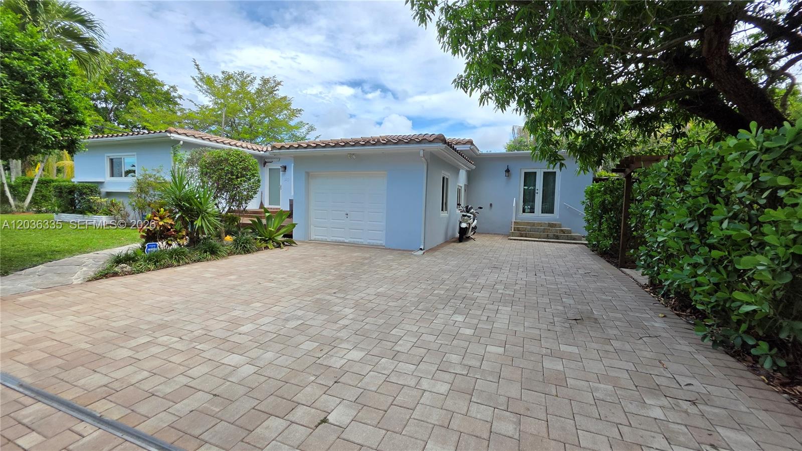 A light blue house features a wooden deck, stone walkway, and lush tropical landscaping — 390 NE 127th St, North Miami FL 33161, NORTH MIAMI, FL