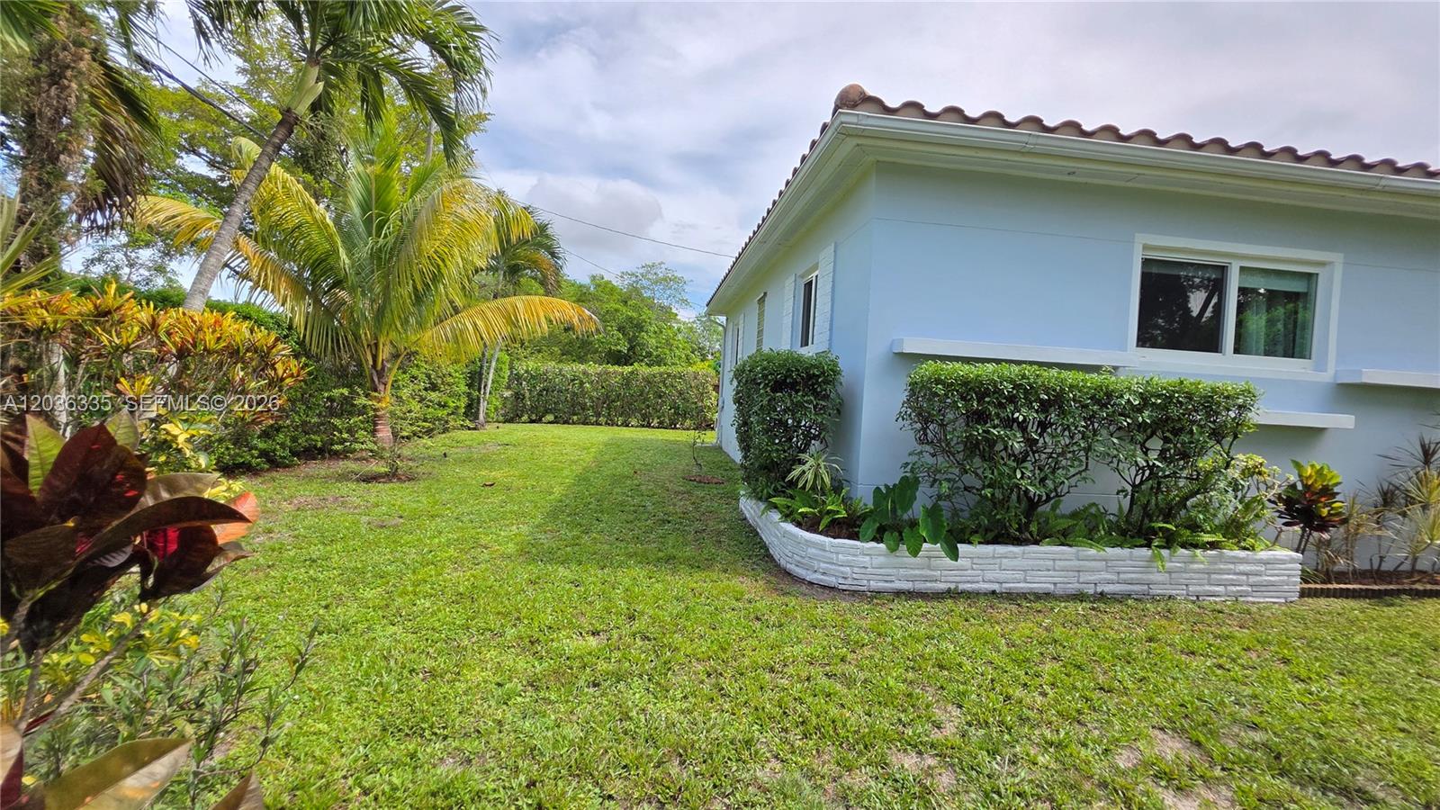 A light blue house exterior features a white brick garden border and surrounding green landscaping — 390 NE 127th St, North Miami FL 33161, NORTH MIAMI, FL