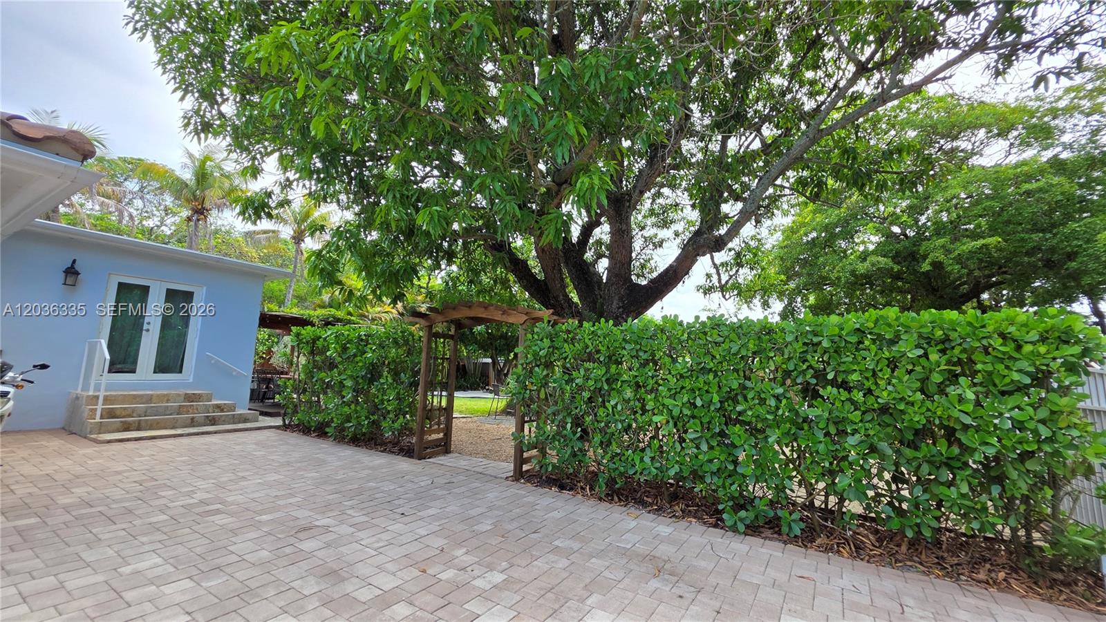 A paved patio features a wooden arbor leading to a backyard with a large tree — 390 NE 127th St, North Miami FL 33161, NORTH MIAMI, FL