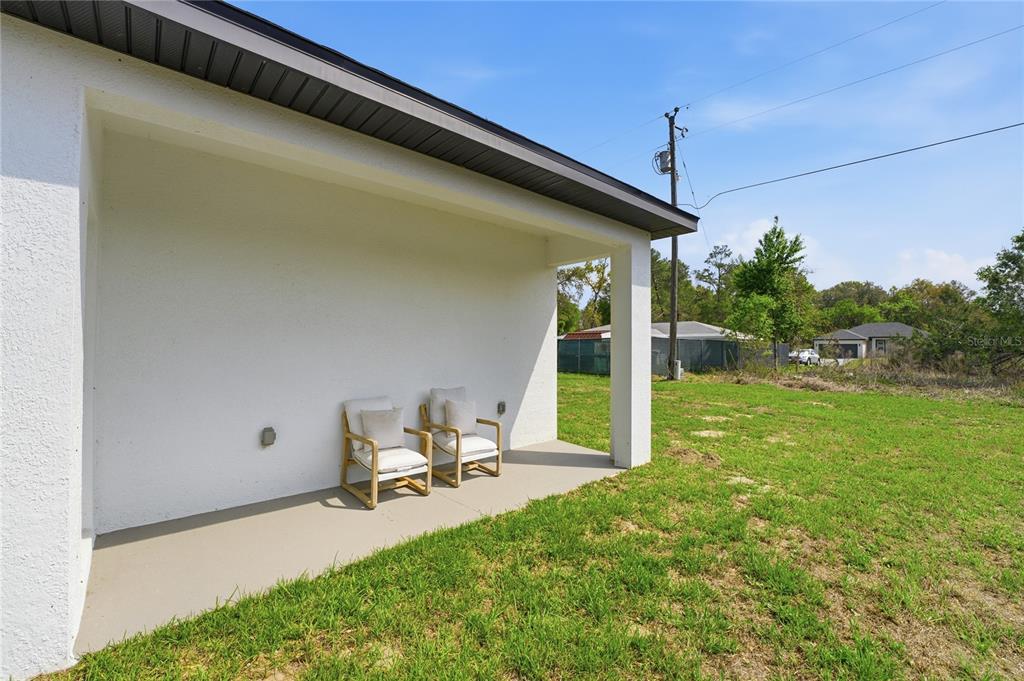 A covered concrete patio features two chairs against a white exterior wall — 535 MARION OAKS LANE, OCALA, FL