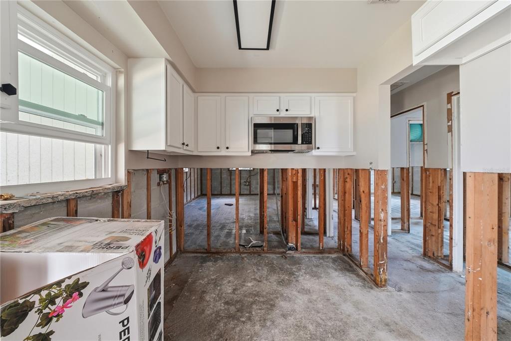A kitchen under renovation features exposed wall studs, concrete flooring, and installed upper cabinets — 7412 S SHERRILL STREET, TAMPA, FL