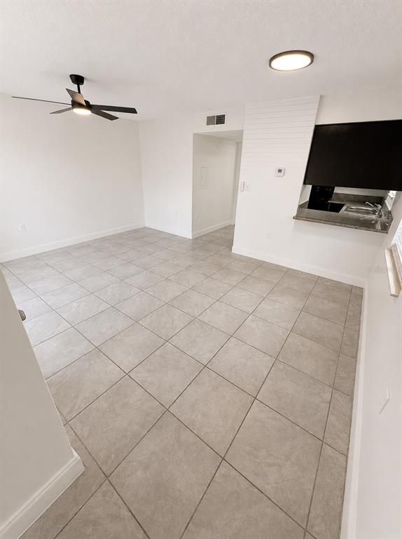 A bright, empty room features light gray tile flooring, a ceiling fan, and a kitchen pass-through — 1185-1185 BENTLEY ROAD UNIT 4, LEESBURG, FL