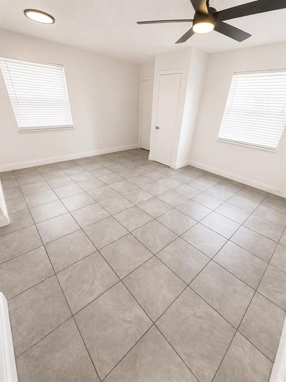 An empty room features gray tile flooring, white walls, two windows, and a ceiling fan — 1185-1185 BENTLEY ROAD UNIT 4, LEESBURG, FL