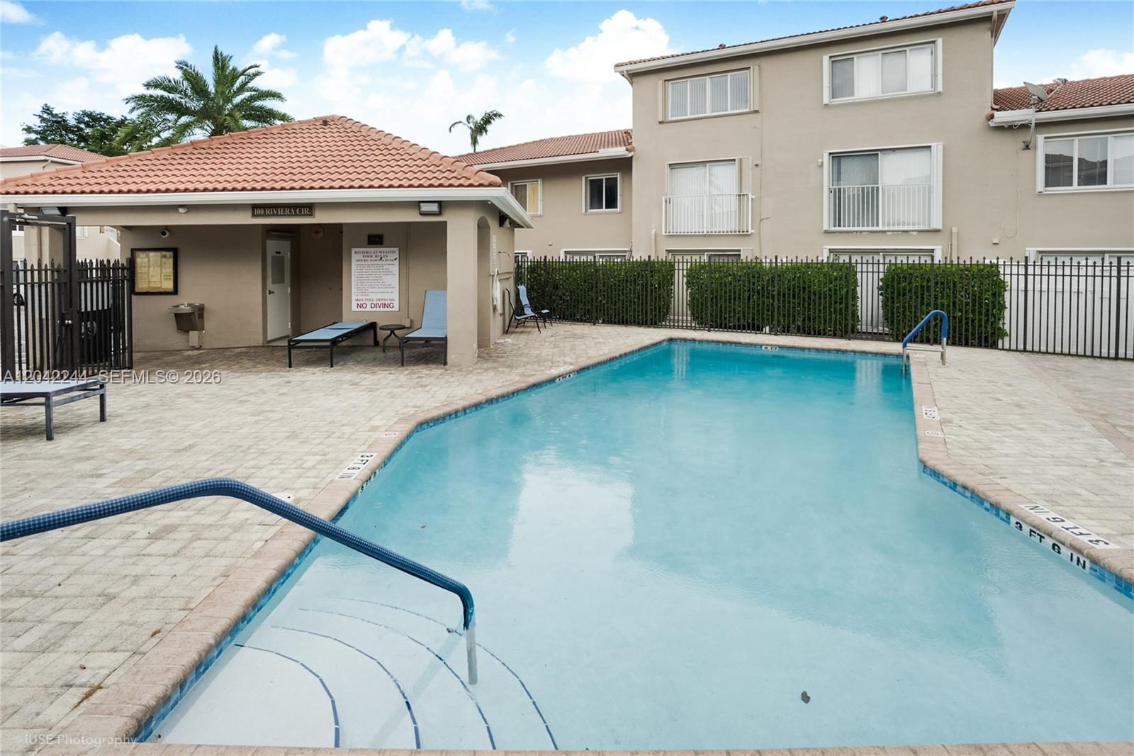 A swimming pool with a blue handrail sits beside a covered patio and apartment building — 221 Riviera Cir, Weston FL 33326, WESTON, FL