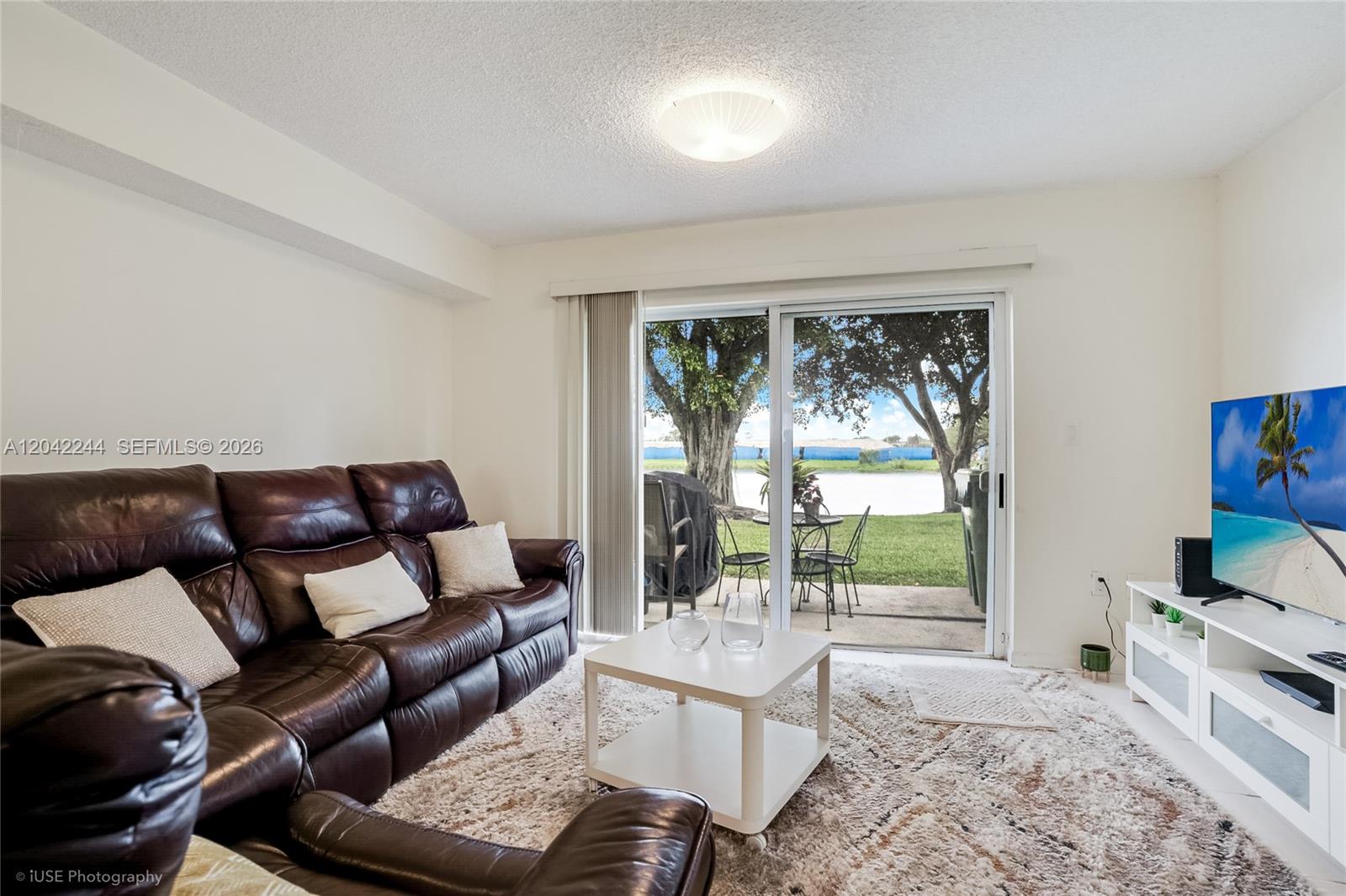A living room features a brown leather sofa, white coffee table, and sliding glass doors — 221 Riviera Cir, Weston FL 33326, WESTON, FL