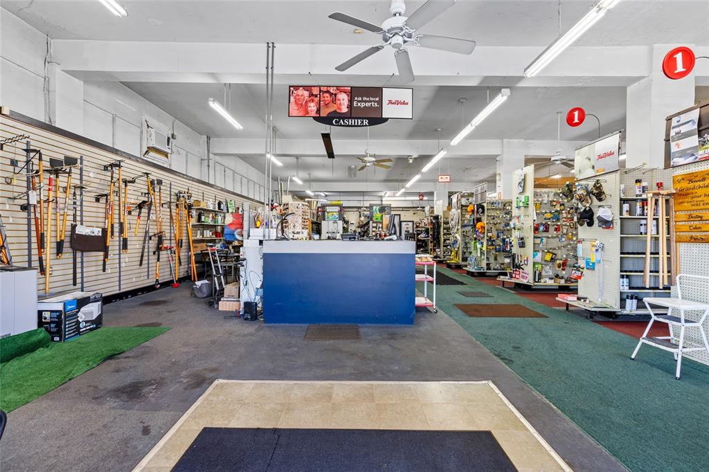 A retail hardware store interior features a central blue cashier counter and wall-mounted tools — 18493 HIGH SPRINGS MAIN STREET, HIGH SPRINGS, FL