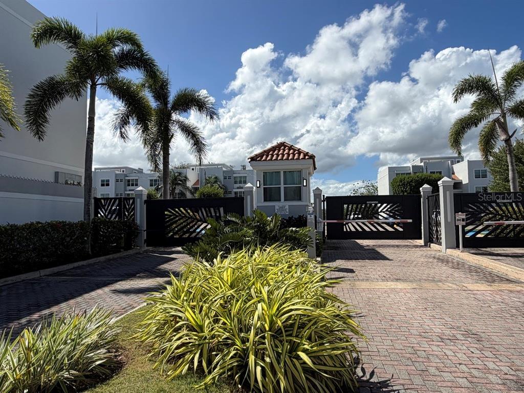 A gated entrance with a guardhouse, palm trees, and brick-paved driveway under a blue sky — 208 COND. VEREDAS DEL MAR UNIT 208, VEGA BAJA, PR
