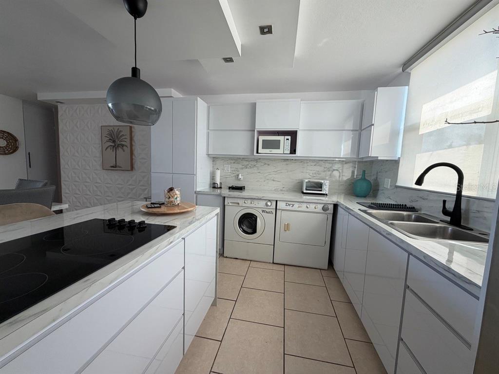 A modern kitchen features white cabinetry, marble-look countertops, a built-in washer and dryer, and tile flooring — 208 COND. VEREDAS DEL MAR UNIT 208, VEGA BAJA, PR