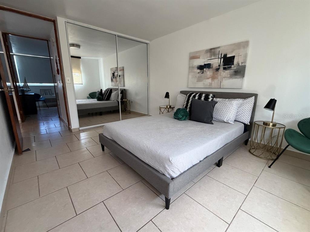 A bedroom features a gray upholstered bed, mirrored closet doors, and light-colored tile flooring — 208 COND. VEREDAS DEL MAR UNIT 208, VEGA BAJA, PR