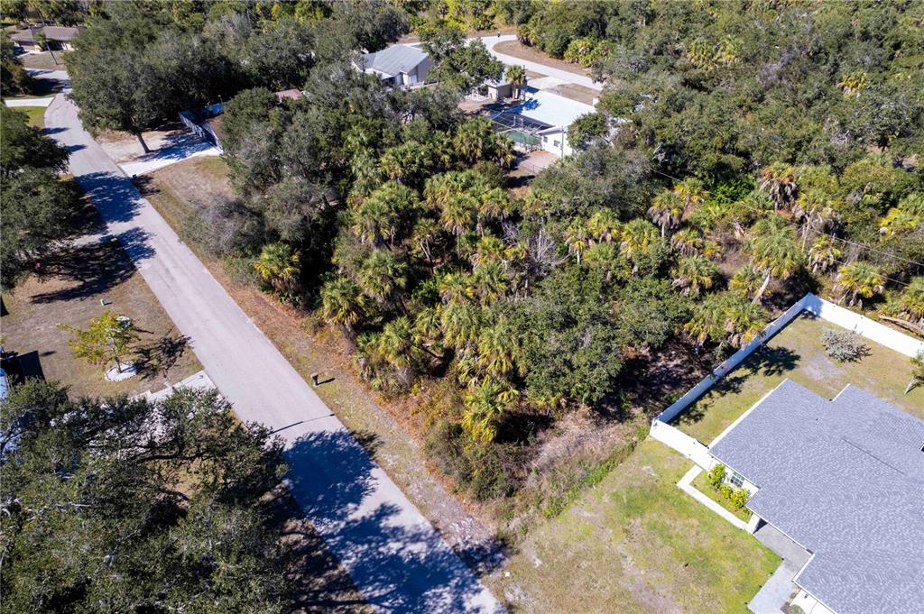 An aerial view shows a vacant, wooded lot situated between two residential properties and a road — 16250 BANYAN AVENUE, PORT CHARLOTTE, FL