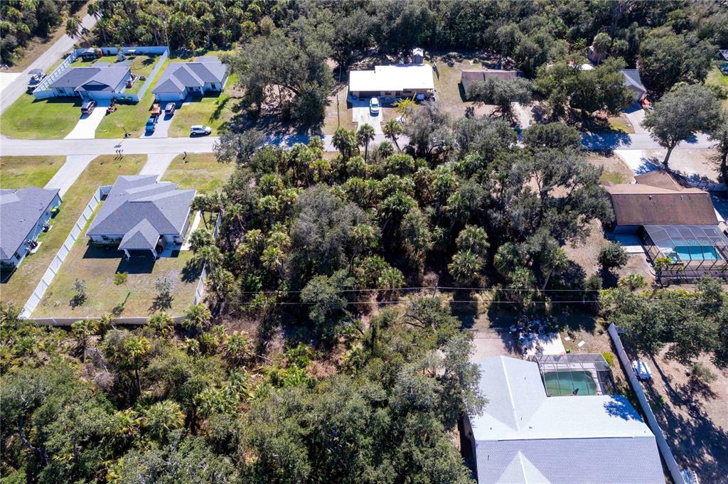 An aerial view shows a wooded residential lot surrounded by houses with pools and driveways — 16250 BANYAN AVENUE, PORT CHARLOTTE, FL