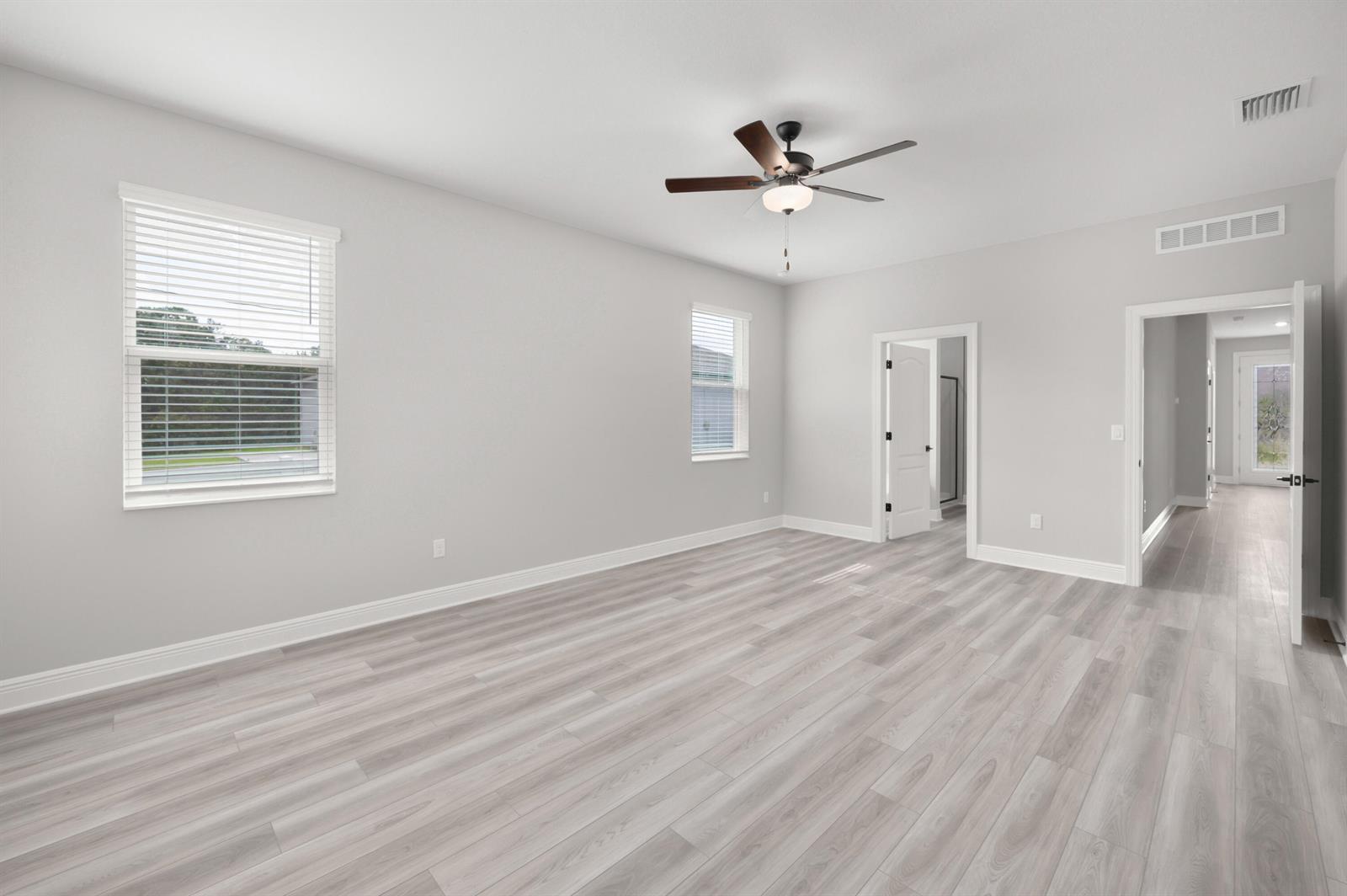 An empty bedroom features light gray walls, wood-look flooring, a ceiling fan, and two windows — 9345 101st Avenue, Vero Beach FL 32967, VERO BEACH, FL