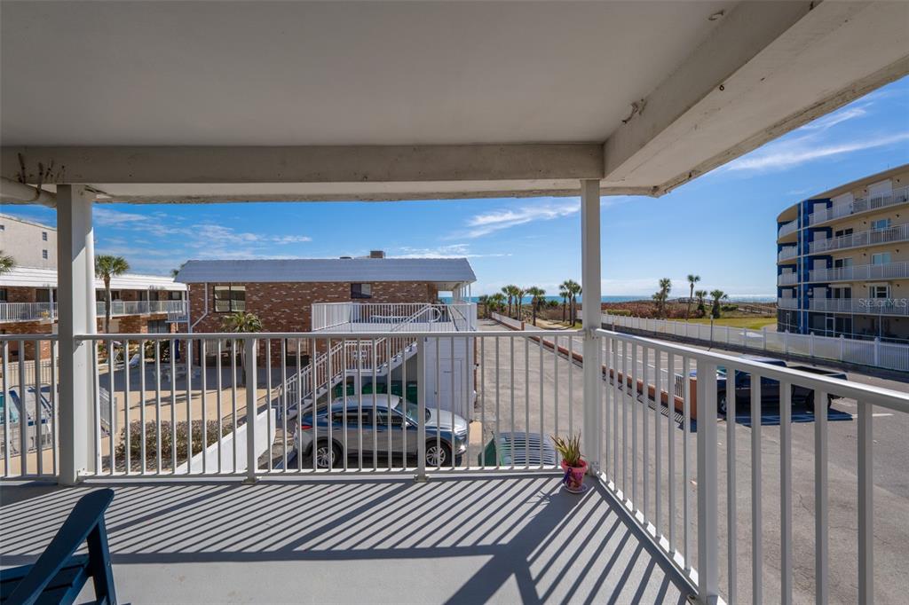 A view from a covered balcony overlooking a parking lot, nearby buildings, and the ocean — 5000 OCEAN BEACH BOULEVARD UNIT B11, COCOA BEACH, FL