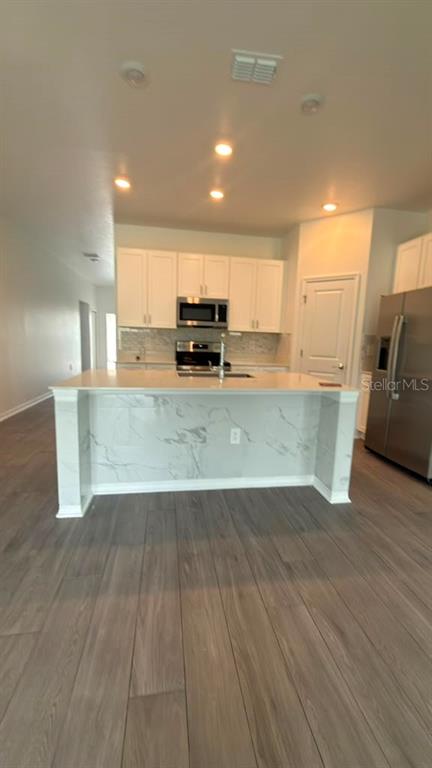 A kitchen features white cabinets, a marble-patterned island, and light wood-look flooring — 707 GROVE STREET, WINTER HAVEN, FL