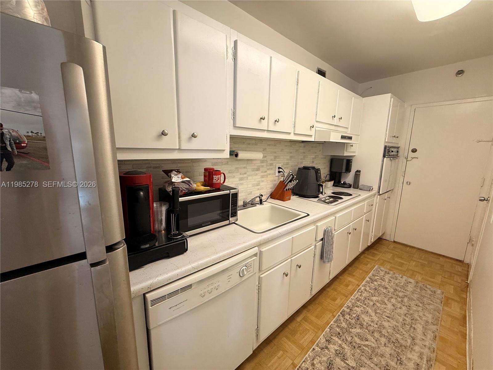 A galley kitchen features white cabinets, stainless steel appliances, and a light-colored countertop — 100 Lincoln Rd # 1512, Miami Beach FL 33139, MIAMI BEACH, FL