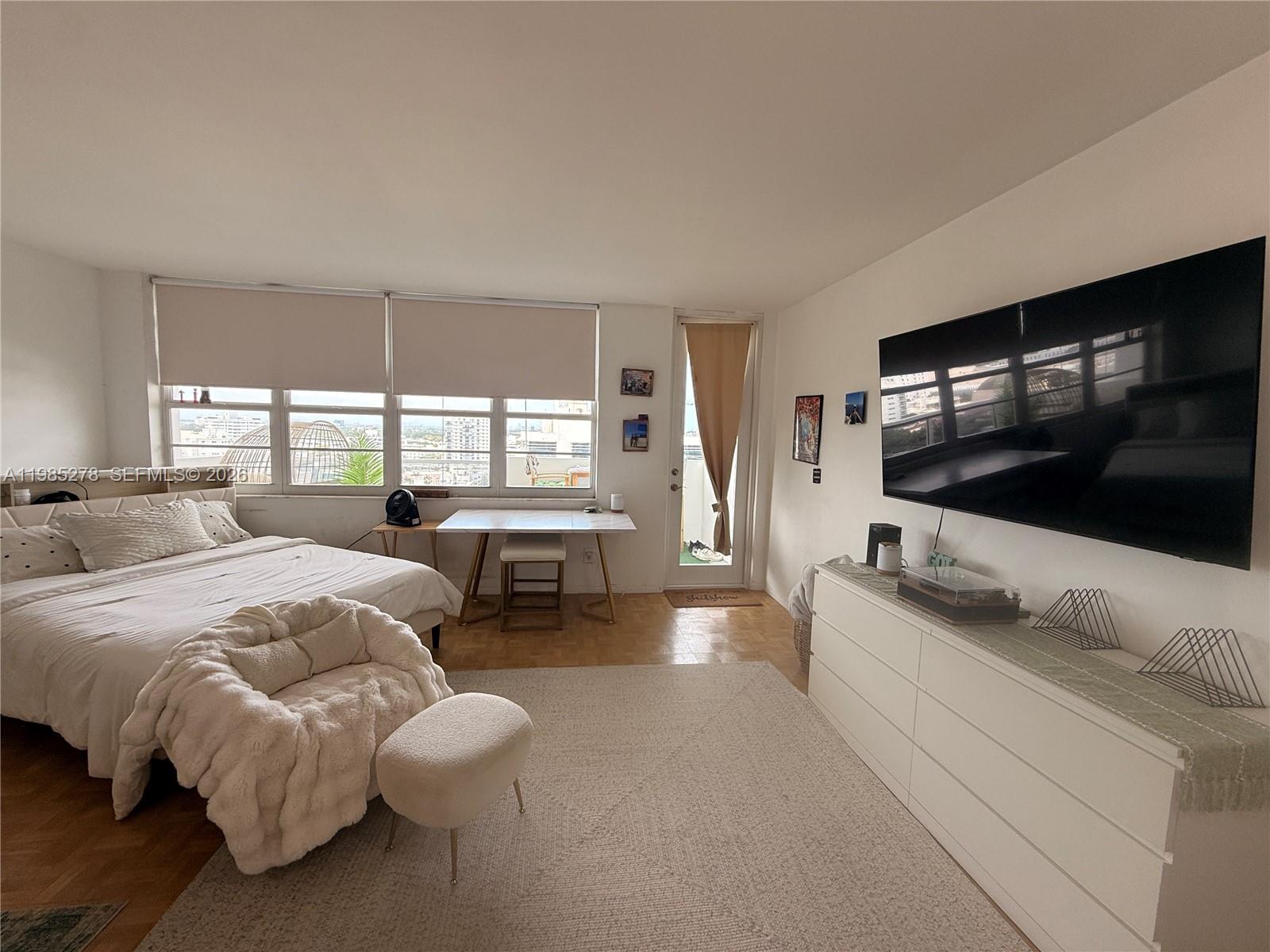A bedroom features a bed, a desk, a dresser with a television, and a balcony door — 100 Lincoln Rd # 1512, Miami Beach FL 33139, MIAMI BEACH, FL