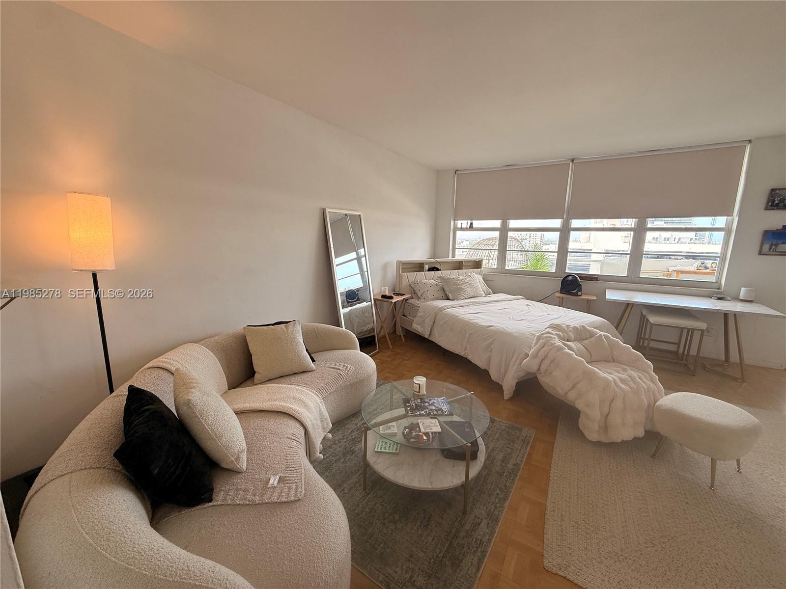 A studio apartment features a curved sofa, a bed, and a desk near large windows — 100 Lincoln Rd # 1512, Miami Beach FL 33139, MIAMI BEACH, FL