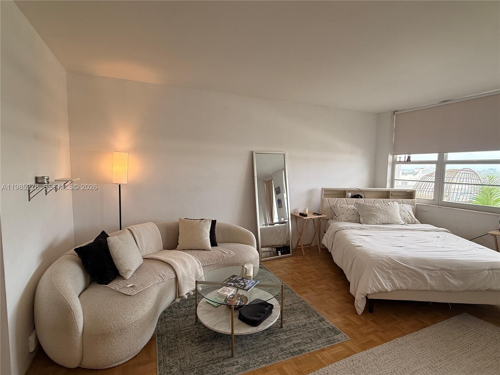 A studio apartment features a curved sofa, a bed, and a floor mirror on parquet floors — 100 Lincoln Rd # 1512, Miami Beach FL 33139, MIAMI BEACH, FL
