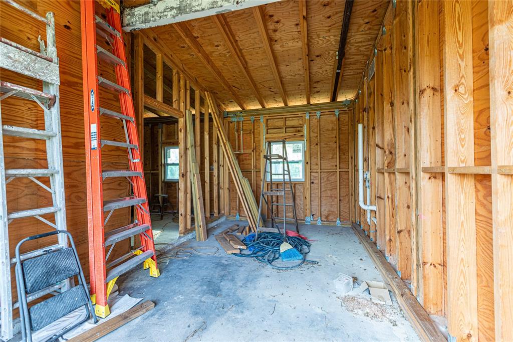 An unfinished room with exposed wood wall studs, plywood sheathing, and ladders on a concrete floor — 4867 LOS RIOS STREET, NORTH PORT, FL