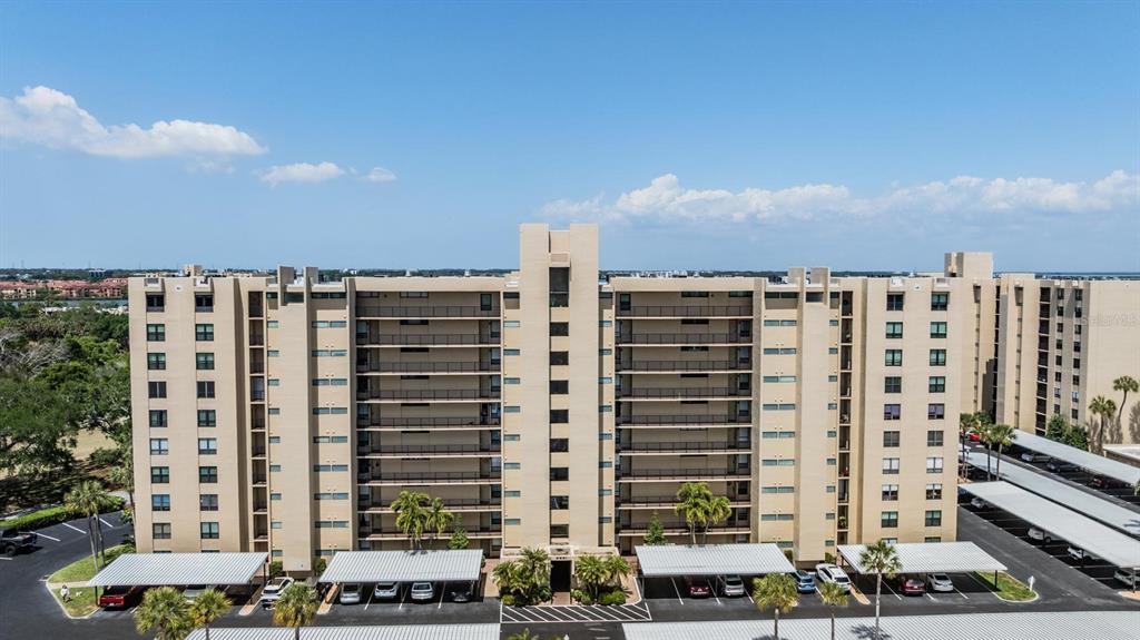An aerial view of a multi-story tan apartment building with covered parking spaces below — 2621 COVE CAY DRIVE UNIT 606, CLEARWATER, FL