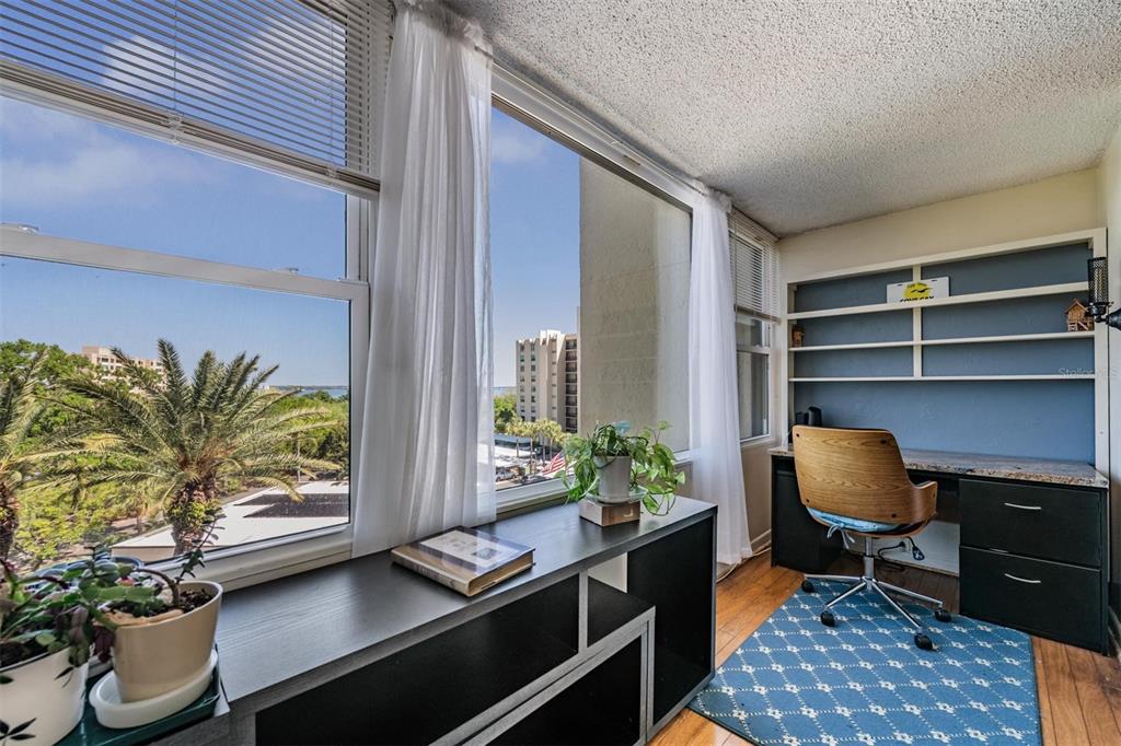 A home office features a desk, shelving, a window with a view, and wood flooring — 2621 COVE CAY DRIVE UNIT 606, CLEARWATER, FL