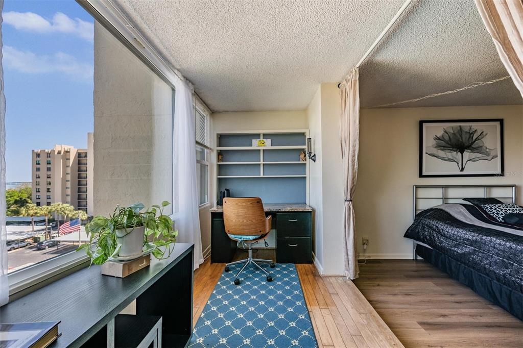 A bedroom with a desk area, a bed, and a large window overlooking a city street — 2621 COVE CAY DRIVE UNIT 606, CLEARWATER, FL