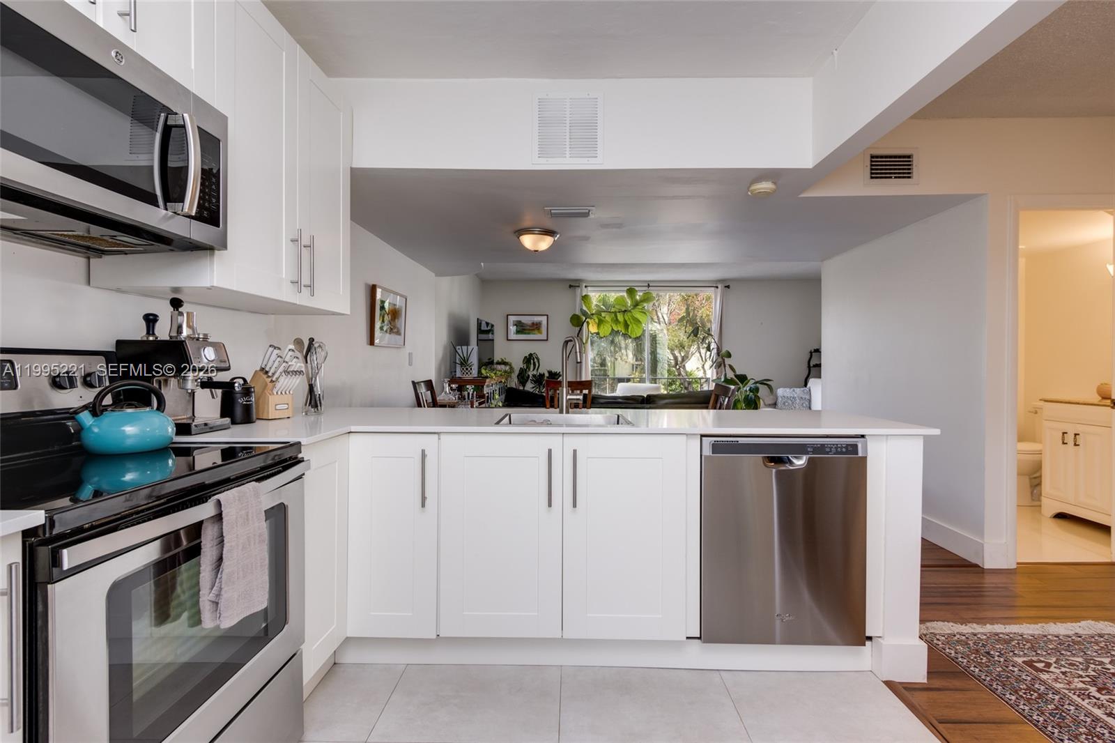 A modern kitchen features white cabinets, stainless steel appliances, and a view into the living area — 1651 NE 115th St # 28C, Miami FL 33181, MIAMI, FL