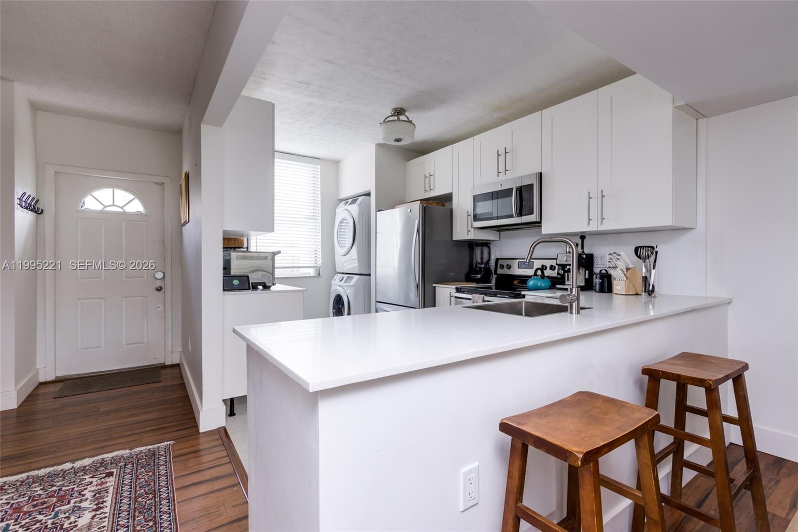 A kitchen features white cabinetry, stainless steel appliances, a breakfast bar, and a stacked washer-dryer — 1651 NE 115th St # 28C, Miami FL 33181, MIAMI, FL