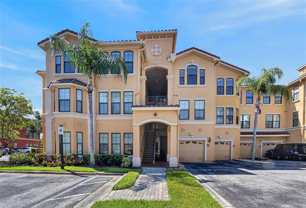 A multi-story tan stucco apartment building features a tiled roof, arched entryway, and attached garages — 2723 VIA CAPRI UNIT 832, CLEARWATER, FL