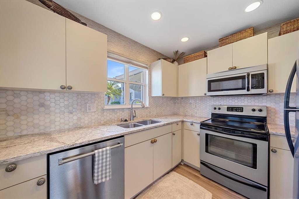 A kitchen features light cabinets, granite countertops, stainless steel appliances, and a hexagonal tile backsplash — 851 AUDUBON DRIVE UNIT 851, BRADENTON, FL