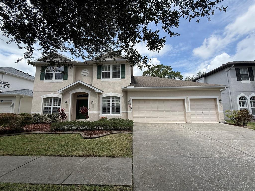 A two-story suburban house with a beige stucco exterior, green shutters, and a three-car garage — 8523 NORTHTON GROVES BOULEVARD, ODESSA, FL