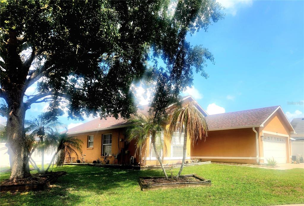 A single-story house with a tan stucco exterior, a two-car garage, and a front lawn — 2483 SHELBY CIRCLE, KISSIMMEE, FL