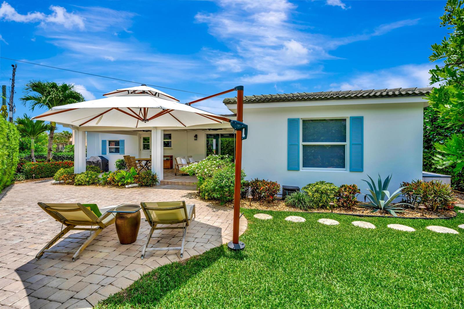 A patio with lounge chairs and a large umbrella sits outside a white house — 333 Ocean Drive, Juno Beach FL 33408, JUNO BEACH, FL