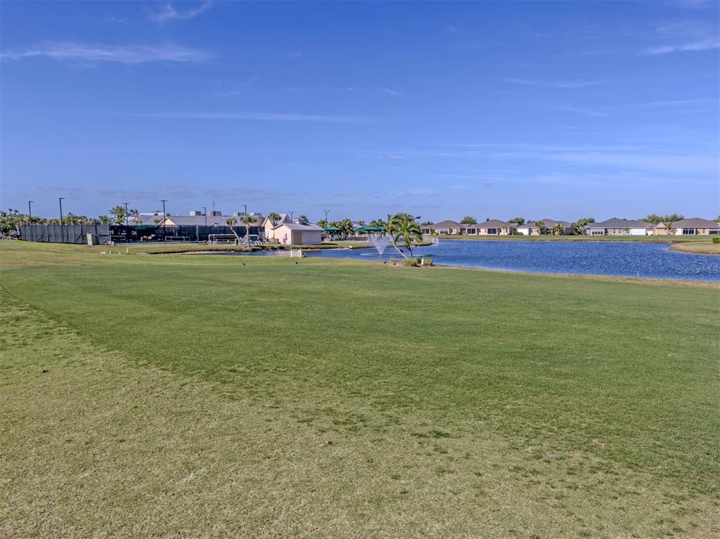 A grassy field overlooks a pond with a fountain and residential houses in the distance — 1799 NOTTINGHAM TRAIL, PUNTA GORDA, FL