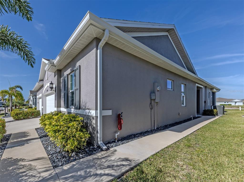 The exterior side view of a gray house features a concrete walkway and landscaping — 1799 NOTTINGHAM TRAIL, PUNTA GORDA, FL