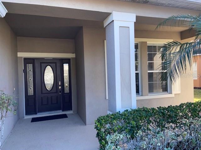 A dark front door with glass inserts sits under a covered porch next to a column — 842 SUSSEX DRIVE, DAVENPORT, FL
