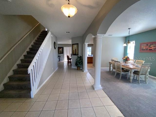 A foyer with a staircase leads to a dining area with tile and carpeted flooring — 842 SUSSEX DRIVE, DAVENPORT, FL